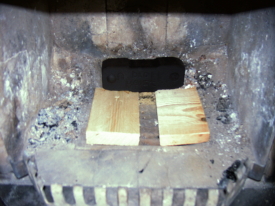 Kaminofen-Beschickung Bild 1: Das teilweise abgedeckte Kaminofen-Rost beschleunigt den Luftstrom zum Anheizen. Das optionale Brikett sorgt für eine gleichmäßigere hohe Wärmeleistung.