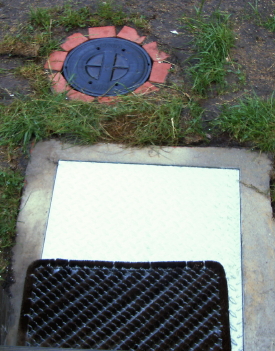 Zisternen-Zugang über eine abhebbare Metallplatte und im Hintergrund der Rewalux® WISY Wirbel-Fein-Filter-Gehäusedeckel.